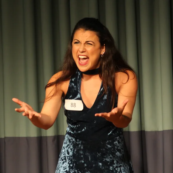 An actor singing with both hands open and stretched toward the audience