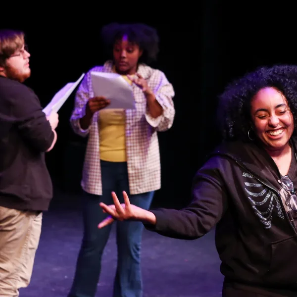 Three actors onstage with scripts in their hands