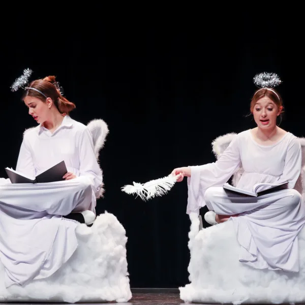 Two actors, costumed like angels, sitting in fluffy chairs with scripts in their laps